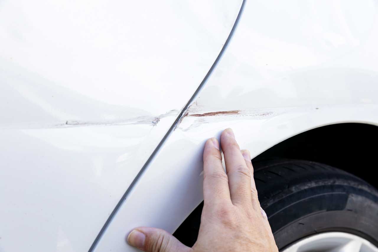 白い車のフェンダー部分にある線状のキズを指先で丁寧に確認している様子