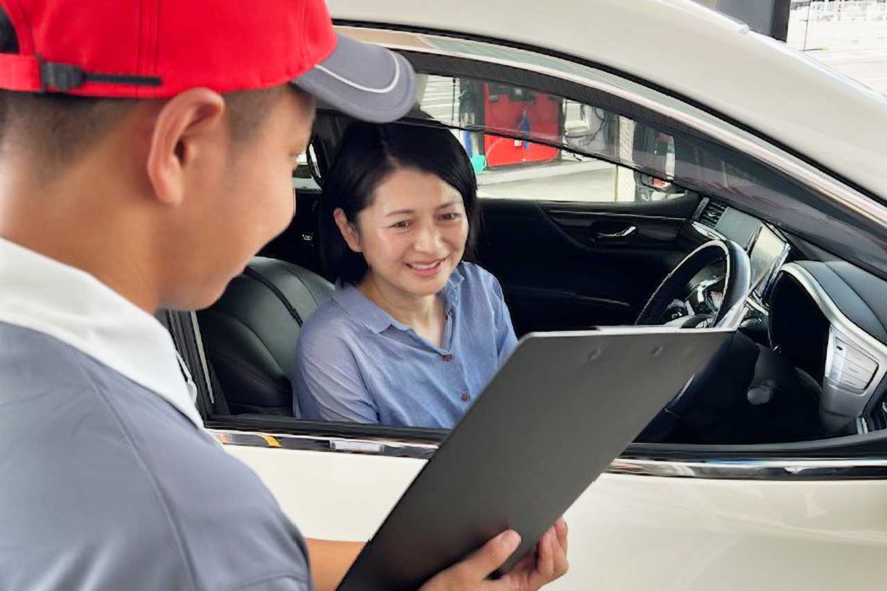 車に乗り込んだお客様と、バインダーを手にして笑顔で直接やり取りをする自社スタッフ