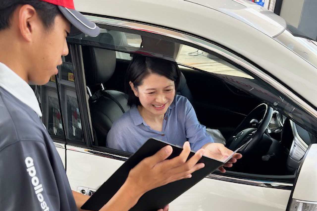 スタッフが車に乗ったお客様にバインダーを見せながら車検の立ち会い見積もりを説明している様子