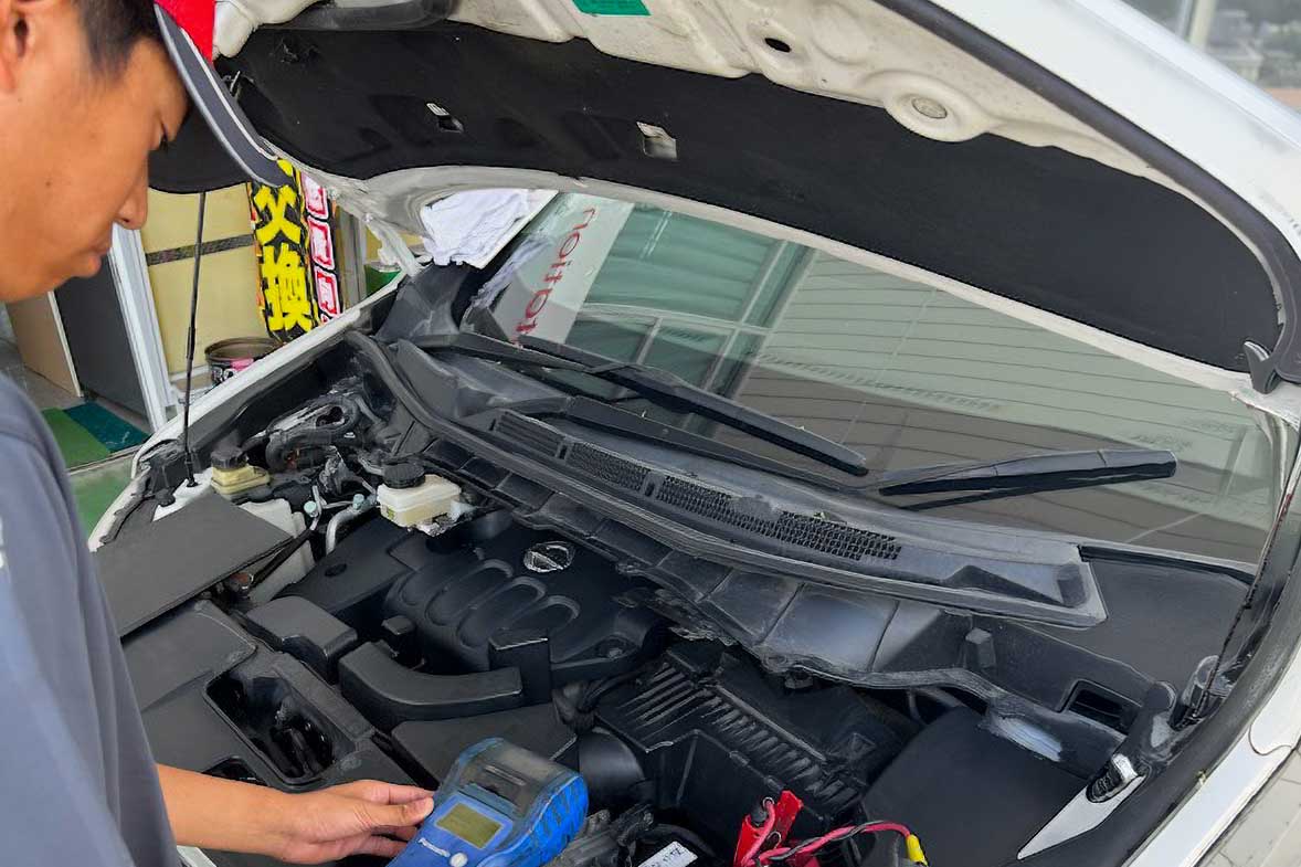ボンネットを開けた車の前で、専用の診断機器を用いて丁寧に車の状態を確認している整備士